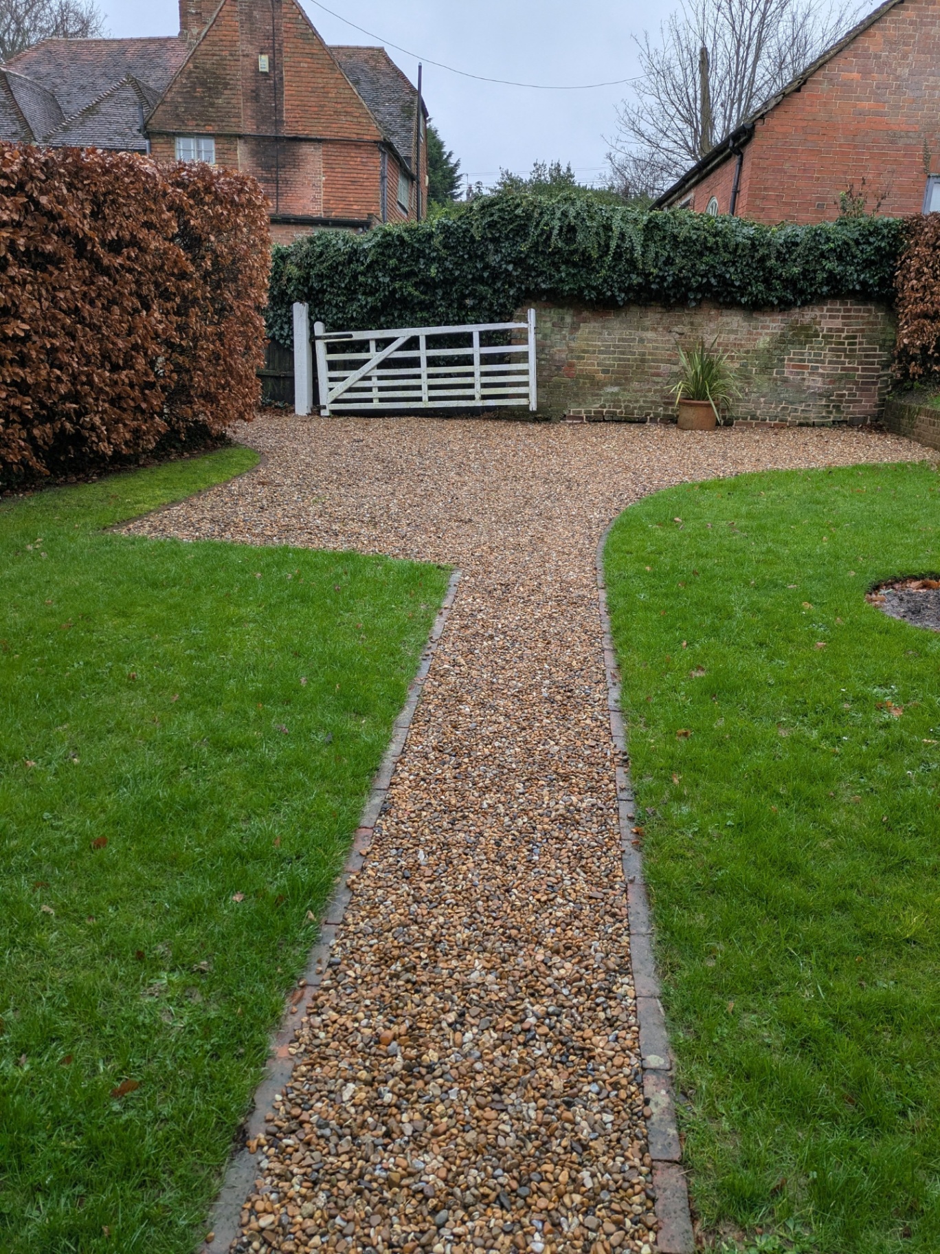 Gravel driveway and path with brick edging leading to a white five-bar gate