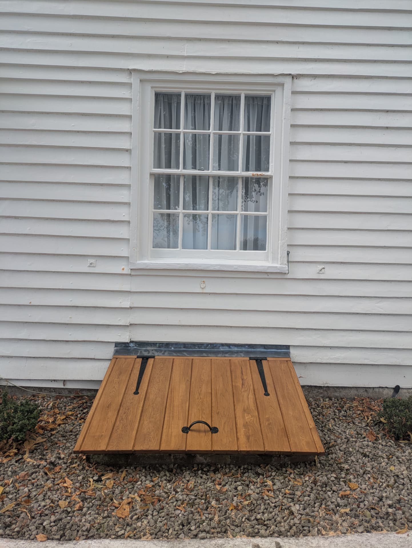 Handmade oak cellar door with wrought iron strap hinges set into a weatherboarded wall